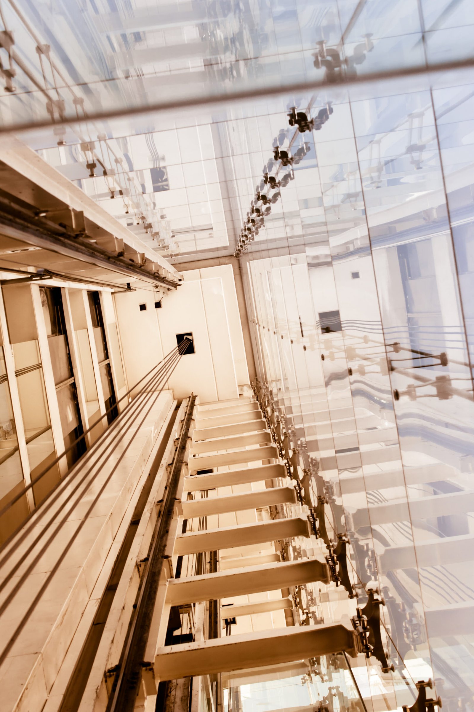 Looking up a glass elevator hoistway with guide rails and structural steel